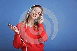 Portrait of beautiful young woman listening to music on color background