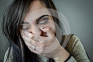 Portrait of a beautiful young woman with long brown hair covering her mouth as she bursts out laughing