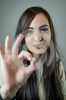 Portrait of a beautiful young woman with long brown hair gesturing ok with her hand while smiling