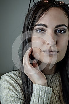 Portrait of a beautiful young woman with long brown hair with her hand on her cheek while she is staring