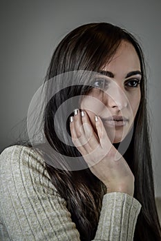 Portrait of a beautiful young woman with long brown hair with her hand on her cheek while she is thinking