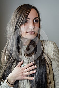 Portrait of a beautiful young woman with long brown hair with her hand on her chest looking intently to her left