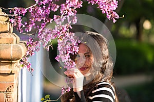 Portrait of a beautiful young woman with long brown hair wearing a black and white striped shirt, hiding among a tree branch with