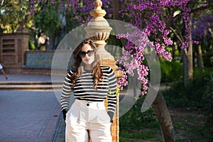 Portrait of a beautiful young woman with long brown hair, wearing a black and white striped shirt, leaning against a column in the