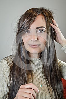 Portrait of a beautiful young woman with long brown hair who is smiling and arranging her hair