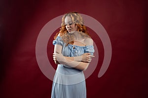 Portrait of a beautiful young woman with long curly red hair, dressed in a fashionable light light blue dress