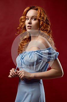 Portrait of a beautiful young woman with long curly red hair, dressed in a fashionable light light blue dress