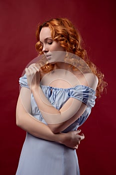 Portrait of a beautiful young woman with long curly red hair, dressed in a fashionable light light blue dress