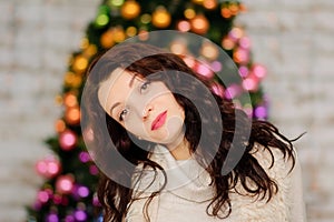 Portrait of Beautiful Young Woman with Long Dark Hair near Blurred Christmas Tree with Colorful Glass Balls.