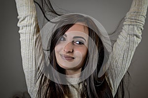 Portrait of a beautiful young woman with long dark hair smiling joyfully with her arms raised