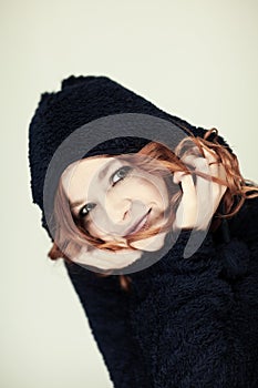 Portrait of a beautiful young woman with long red curly hair and perfect make up, cozy dark winter sweater with hat