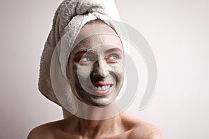 Portrait of beautiful young woman look aside applying clay facial mask, wrap towel on head skin care treatment concept.