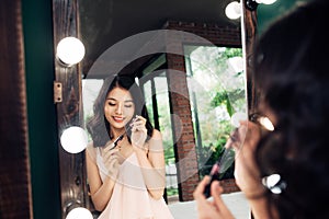 Portrait of beautiful young woman looking at the mirror applying