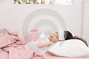 Portrait of a beautiful young woman lying in bed, having a cold and sneezing in a tissue