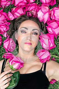 Portrait of a beautiful young woman, she is lying on the grass surrounded by roses. Festive background.