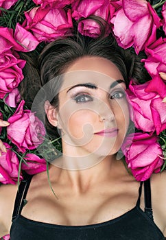 Portrait of a beautiful young woman, she is lying on the grass surrounded by roses. Festive background.