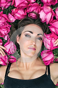 Portrait of a beautiful young woman, she is lying on the grass surrounded by roses. Festive background.