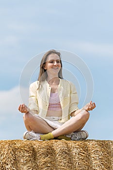 Portrait of beautiful young woman meditating sitting in the hay against blue sky. Unity with nature