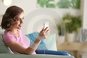 Portrait of beautiful young woman with mobile phone listening to music at home