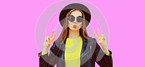 Portrait of beautiful young woman model blowing her lips sends air kiss wearing black round hat isolated on pink background