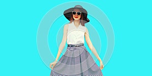 Portrait of beautiful young woman model posing wearing black summer straw round hat and striped skirt isolated on blue background