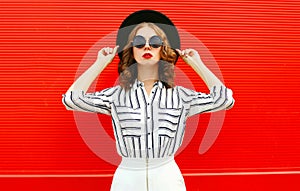 Portrait beautiful young woman model wearing white striped shirt, black round hat posing over red wall