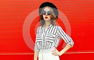 Portrait beautiful young woman model wearing white striped shirt, black round hat posing over red wall