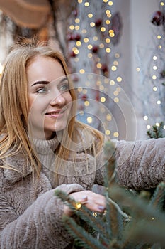 Portrait of beautiful young woman near the Christmas decorations standing outdoors. Christmas mood, holidays. Vertical frame