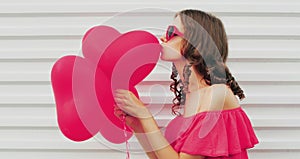 Portrait beautiful young woman with pink heart shaped balloon blowing her lips sending sweet air kiss on a white background