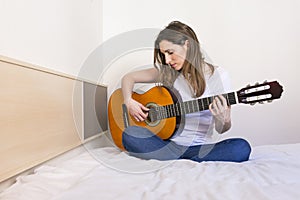 Portrait of a beautiful young woman playing guitar at home and h