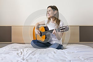 Portrait of a beautiful young woman playing guitar at home and h