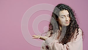 Portrait of beautiful young woman pointing sidewards and smiling on pink background