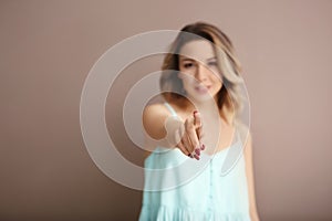 Portrait of beautiful young woman pointing at viewer on color background