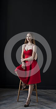 Portrait of a young woman in a red dress sitting on a high bar stool