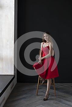 Portrait of a young woman in a red dress sitting on a high bar stool