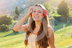 Portrait of beautiful young woman with red flower on ear with natural background looks at camera in spring time