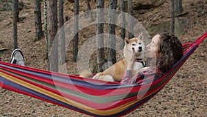 Portrait of beautiful young woman relaxing in hammock in autumn forest kissing shiba inu dog