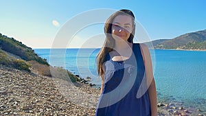 Portrait of beautiful young woman running hand through hair blowing in wind on background of mediterranean beach. Slow