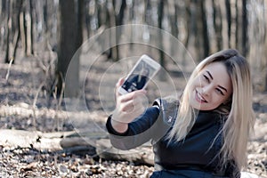 Portrait of a beautiful young woman selfie in the park with a smartphone doing v sign