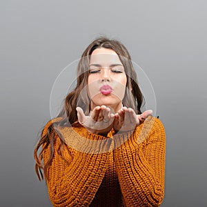 Portrait of beautiful young woman sending kiss against gray background