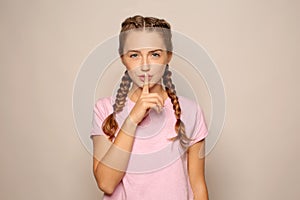 Portrait of beautiful young woman showing silence gesture on light background