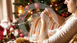 Portrait of beautiful young woman sitting in armchair next to CHristmas tree and knitting