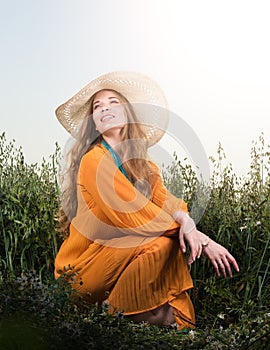Portrait of beautiful young woman sitting in the grass. Hat and red dress