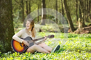 Portrait of a beautiful young woman smiling and playing guitar outdoors