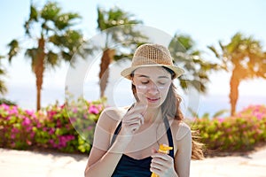 Portrait of a beautiful young woman, smiling in a swimsuit smeared face with sun protection cream in hat on sea