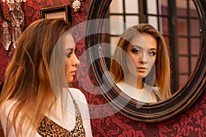 Portrait of a beautiful young woman standing near the mirror looking at his reflection