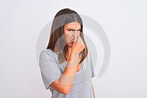 Portrait of beautiful young woman standing over isolated white background smelling something stinky and disgusting, intolerable