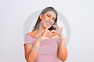Portrait of beautiful young woman standing over isolated white background smiling in love doing heart symbol shape with hands