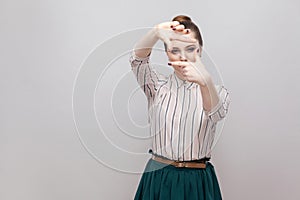 Portrait of beautiful young woman in striped shirt and green skirt with makeup and collected ban hairstyle, standing with cropping