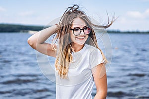 Portrait of a beautiful young woman in stylish glasses. Girl in white tshirt posing on the background of the lake landscape